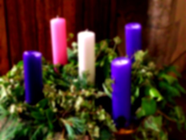 five candles, a white one in the centre, and surrounded by a christmas wreath