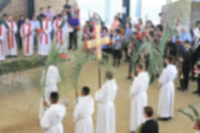 Top down view of a church service. Clergy holding palm leaves and a cross.