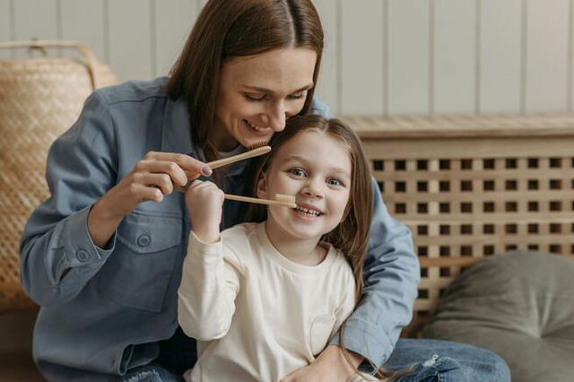 A Woman and a Child With Long Hair Holding Wooden Toothbrushes