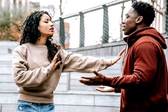 An unhappy couple are breaking up, the woman holds her palms up to the man as he shrugs.