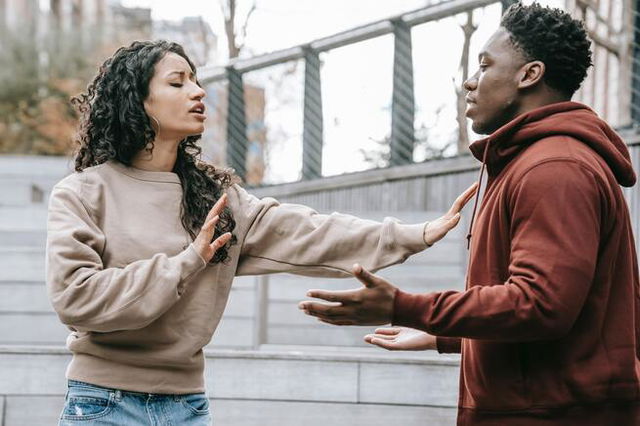 An unhappy couple are breaking up, the woman holds her palms up to the man as he shrugs.