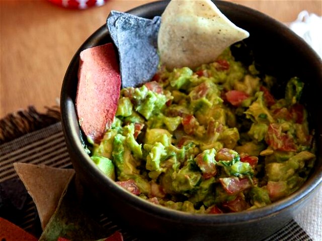 a bowl of guacamole decorated with three triangular chips