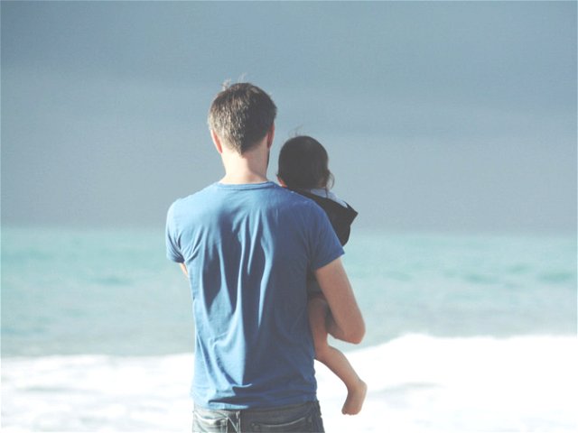 pai com filho ao colo de frente para o mar