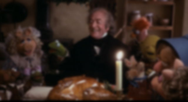 Scrooge surrounded by muppets, all laughing and sharing in Christmas dinner