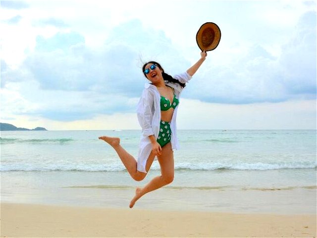 a girl wearing a bikini jumping on the beach