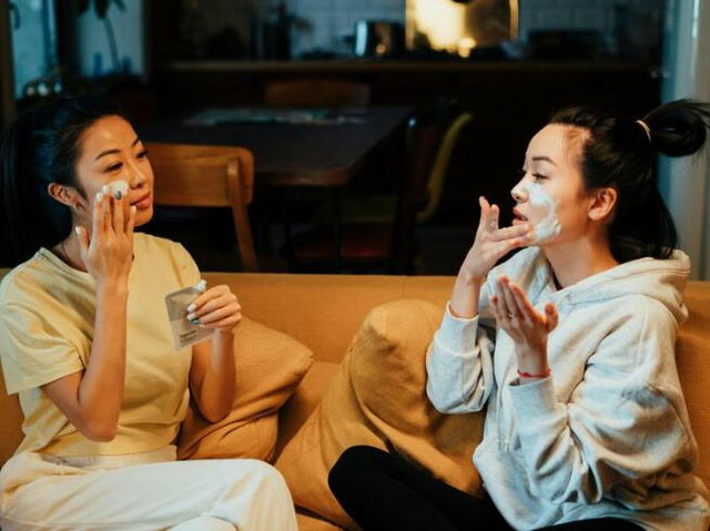 Woman in White Sweater and Black Pants Sitting on Brown Couch Doing Skincare