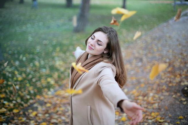 A woman standing alone, eyes closed, arms outstretched, smiling. leaves blowing around her