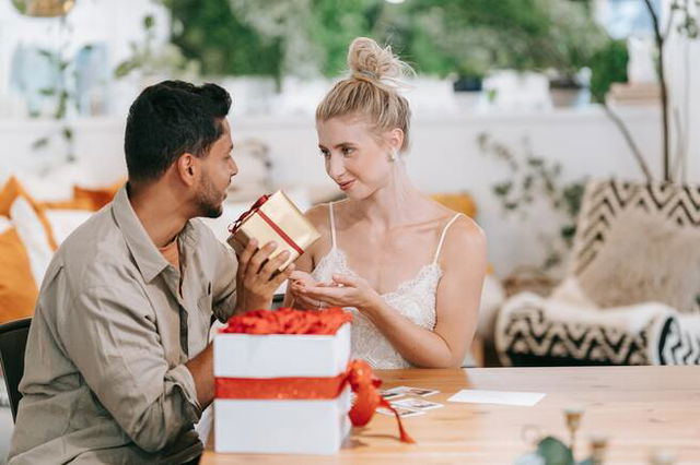 a man and woman sitting at a table and the woman giving a gift to a man