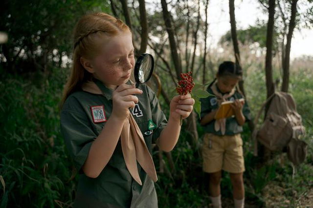 Two girl scouts. One looking through a magnifying glass, the other writing in a journal