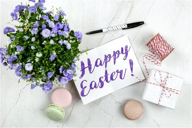 Happy Easter sign surrounded by purple flowers, macaroons, a parcel and a pen