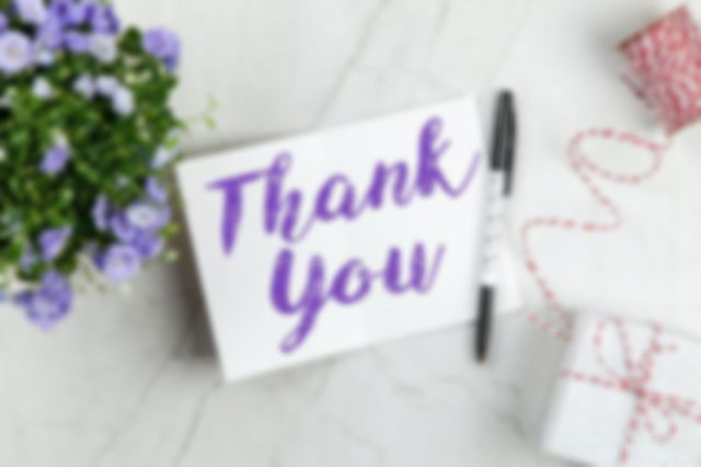 Thank you written on a card next to a bouquet of purple flower, a pen and a small parcel