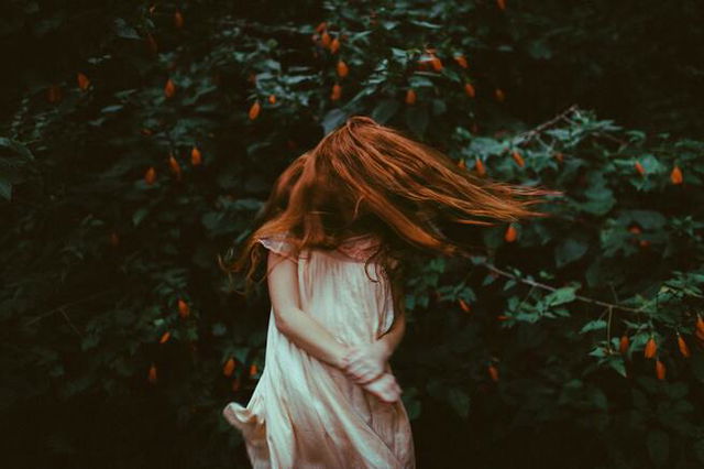 Girl With Red Hair in White Dress Standing in Front of Green Plants