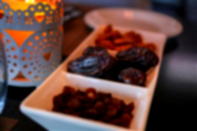 a white rectangular tray holds dates and raisins sat beside a candle in a patterned cup