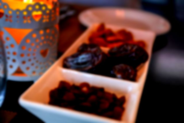 a white rectangular tray holds dates and raisins sat beside a candle in a patterned cup