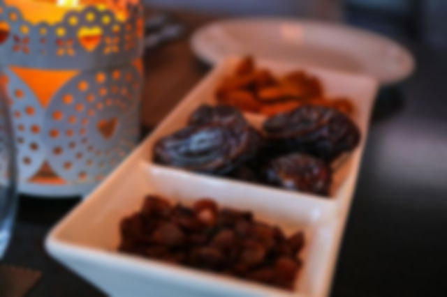 a white rectangular tray holds dates and raisins sat beside a candle in a patterned cup