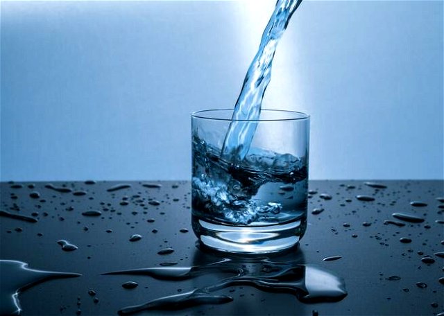 Image of water being poured in a glass surrounded by water droplets and blue background