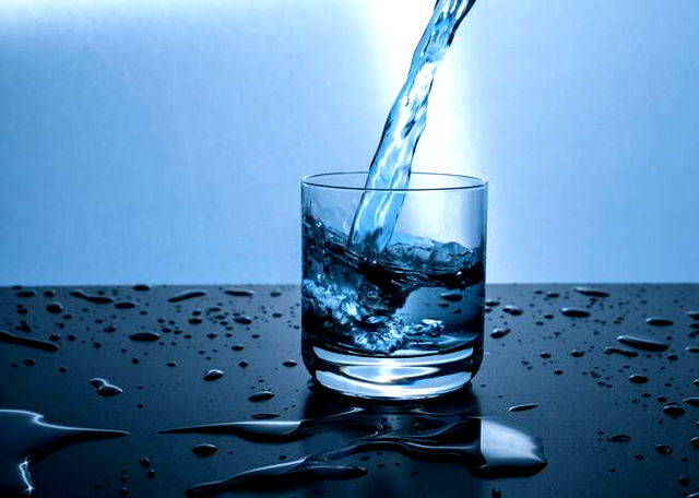 Image of water being poured in a glass surrounded by water droplets and blue background