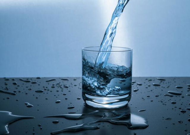 Image of water being poured in a glass surrounded by water droplets and blue background