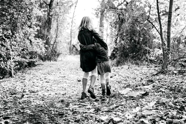 a black and white image of two girls arm in arm walking through the woods