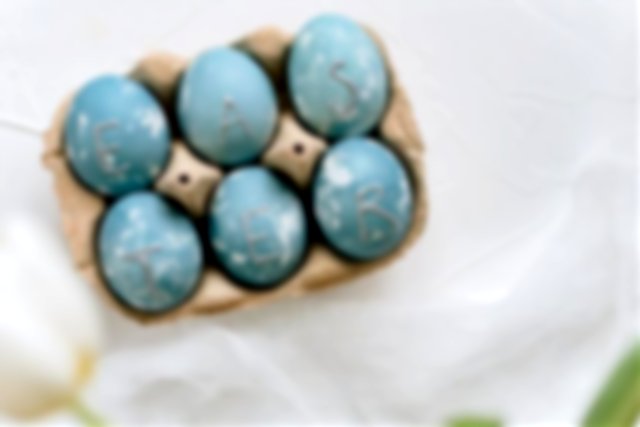 six eggs painted in shades of blue sat in an egg box, silver initials decorate them with the letters EASTE, & R.