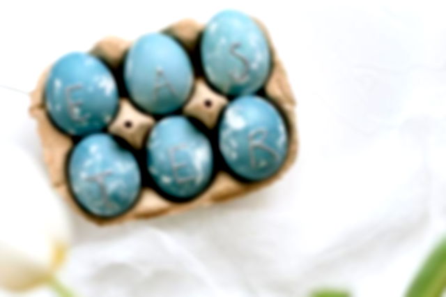 six eggs painted in shades of blue sat in an egg box, silver initials decorate them with the letters EASTE, & R.