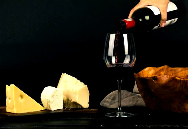 Photo of Person Pouring Wine into Glass besides Some Cheese Pairings