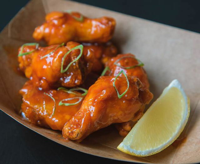 A serving of chicken wings tossed in sauce with a lime wedge