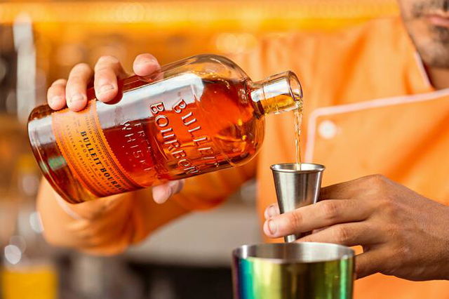 Person Holding a Bottle of Bullet Bourbon and Stainless Jigger