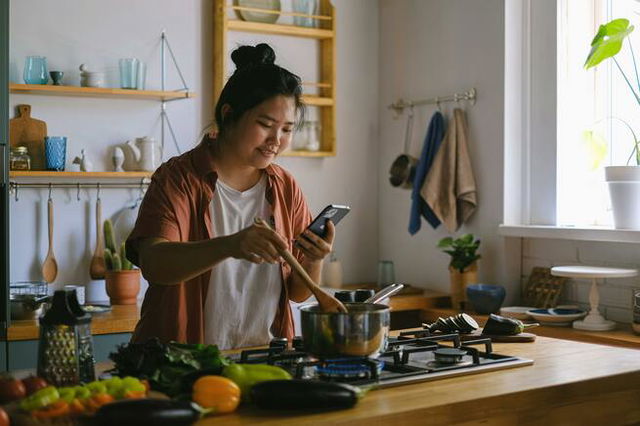 Woman Using a Phone while Cooking in a Kitchen