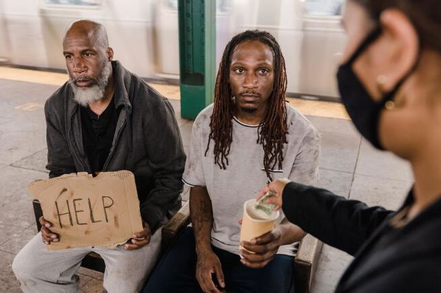 Two men begging for money, one with a sign that says help. Someone is placing money into their cup.