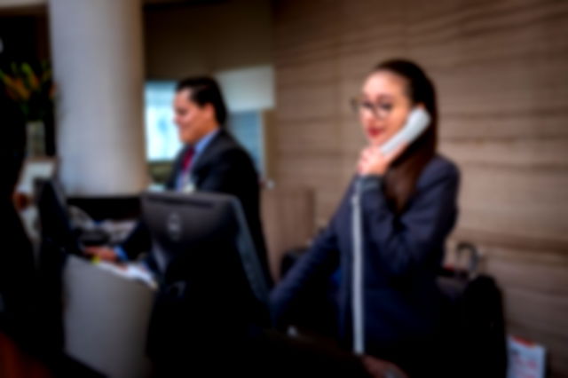 Two receptionists wearing suits, smiling. One on her phone, the other at his computer