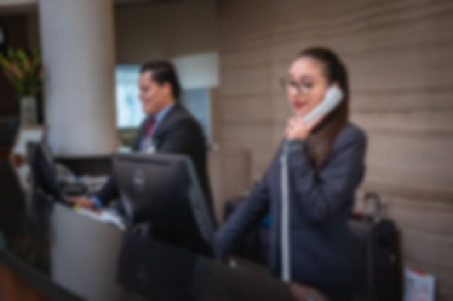 Two receptionists wearing suits, smiling. One on her phone, the other at his computer