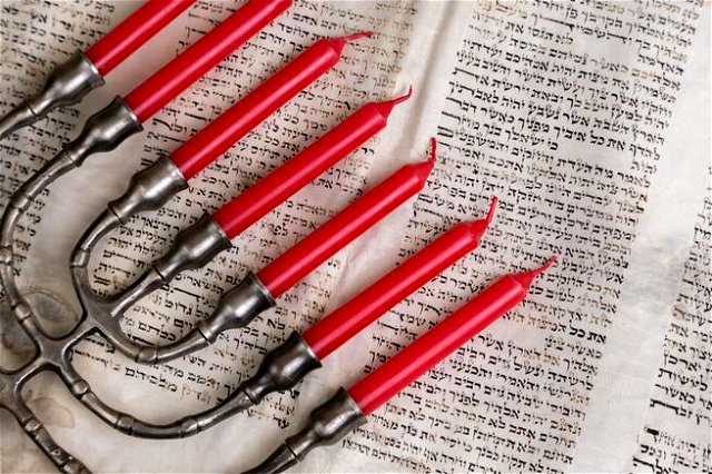 A menora with red candles laying on an open page of the Hebrew Bible.