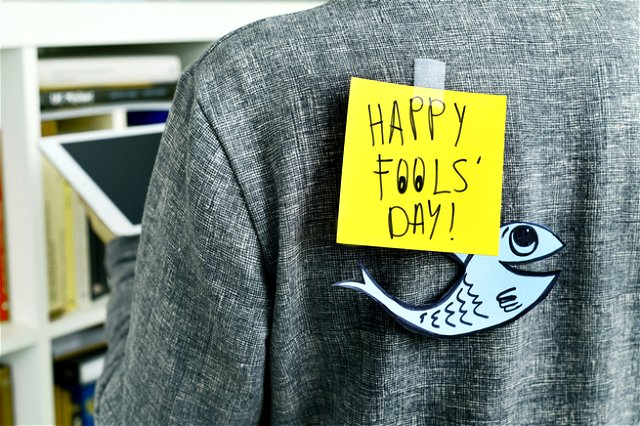 A jacket being worn, attached to their back a post it note that says “Happy Fools’ Day!