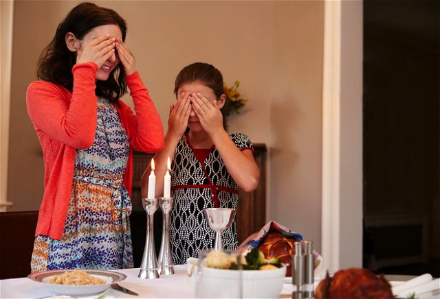 Jewish people cover their eyes after lighting candles to recite a blessing on Shabbat