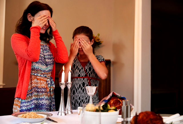 Jewish people cover their eyes after lighting candles to recite a blessing on Shabbat