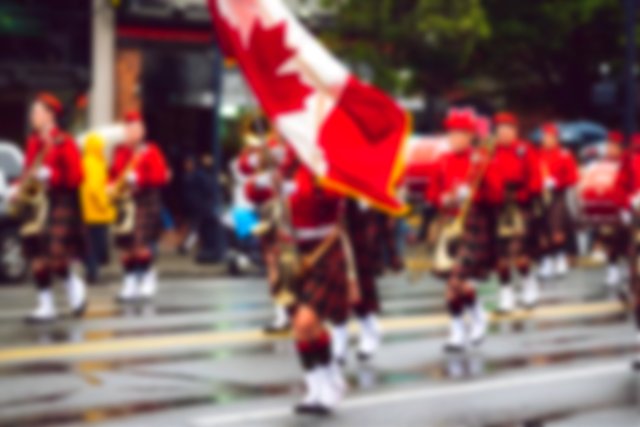 dressed in kilts, holding musical instruments and waving the Canadian flag, a band marches through a city