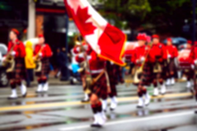 dressed in kilts, holding musical instruments and waving the Canadian flag, a band marches through a city