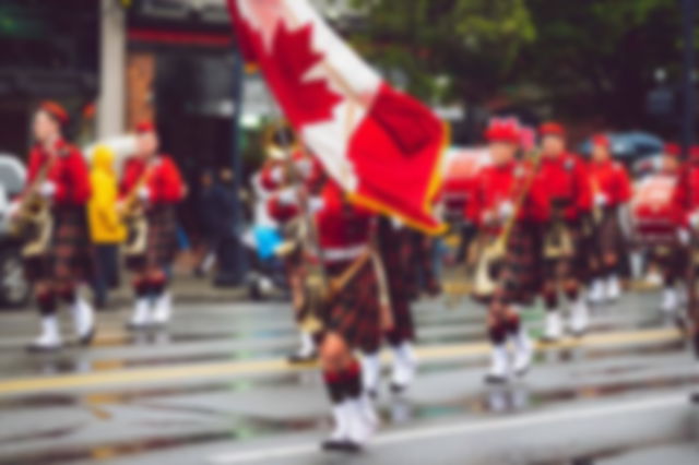 dressed in kilts, holding musical instruments and waving the Canadian flag, a band marches through a city