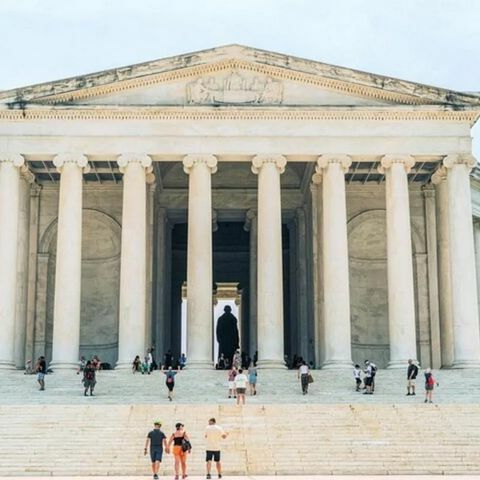 Front view of the Lincoln Memorial with tall white columns, wide steps, and visitors walking up toward the statue inside.