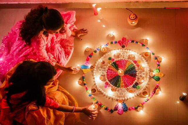 Women Sitting on the Floor Holding diyas Beside Colorful Flowers