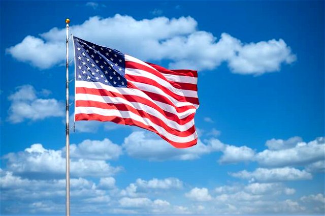 American flag blowing in the wind, a blue sky with thin clouds behind it