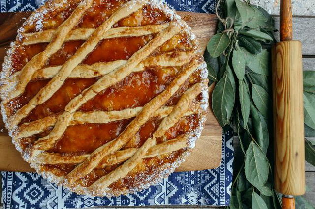 apple pie on a wooden board next to a rolling pin.