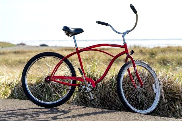 A red old fashioned bike with a grassy background and blue sky