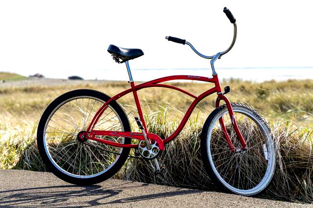 A red old fashioned bike with a grassy background and blue sky