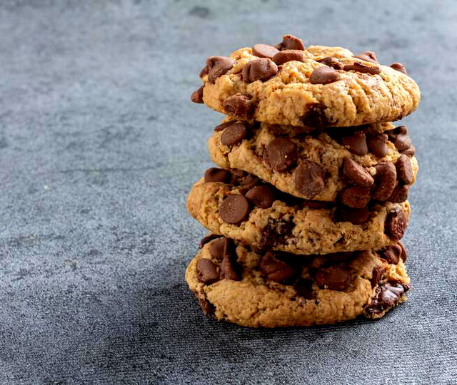 a pile of four thick chocolate chip cookies on a grey carpeted surface