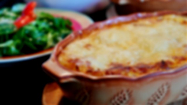 A cottage pie in a ceramic dish, with green vegetables in the background