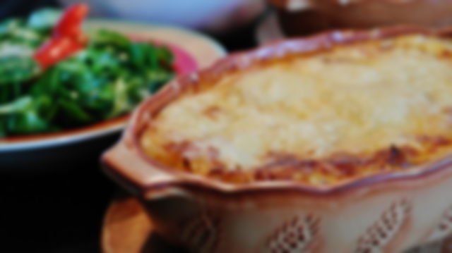 A cottage pie in a ceramic dish, with green vegetables in the background