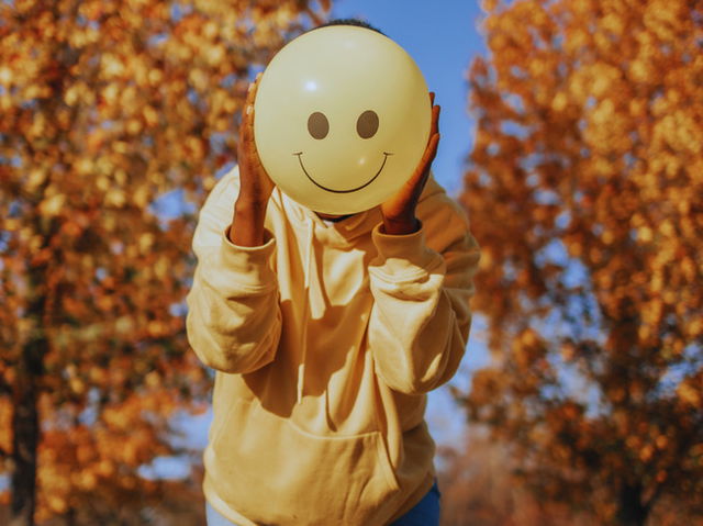 pessoa pousando para foto com bola com cara de emoji à frente do rosto