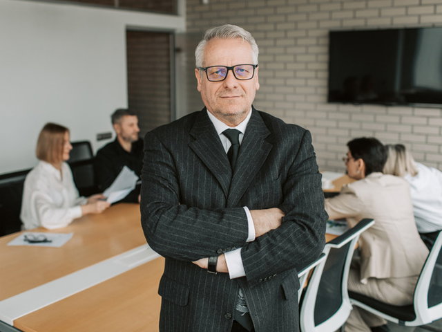 gerente bancário com colegas ao fundo da sala em mesa de reunião